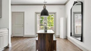 A room with a wooden table, a hanging pendant light, a large mirror, and a view of greenery outside. - Roomy & Walkable to some of CHS Best Music & Food! (Charleston)