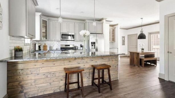 A modern kitchen with white cabinets, a wooden island with stools, stainless steel appliances, and pendant lighting. - Roomy & Walkable to some of CHS Best Music & Food! (Charleston)