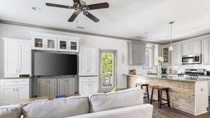 A modern kitchen with white cabinets, a large flat-screen TV, and a wooden island with bar stools. - Roomy & Walkable to some of CHS Best Music & Food! (Charleston)