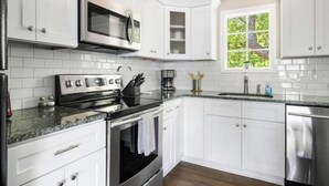 A modern kitchen with white cabinets, stainless steel appliances, and a window with a view of greenery. - Homey Place A Short Drive to Downtown & the Beach (Charleston)