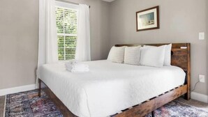 A bedroom with a bed, a window with blinds, a framed picture on the wall, and a patterned rug. - Homey Place A Short Drive to Downtown & the Beach (Charleston)