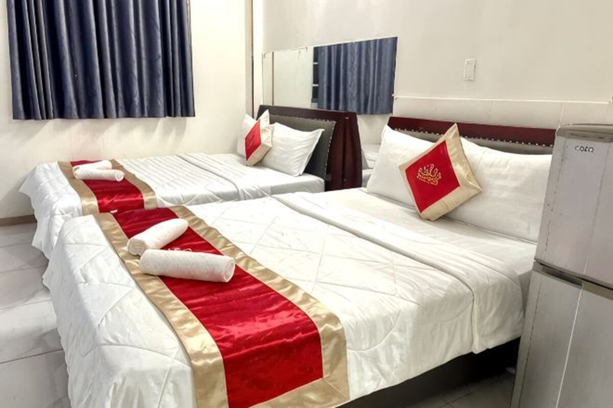 Une chambre d’hôtel avec deux lits, un miroir, un réfrigérateur et une fenêtre avec des rideaux.