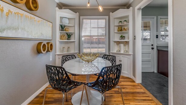 Un comedor con una mesa redonda, sillas negras y estanterías blancas decoradas.