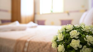 Ein Hotelzimmer mit einem ordentlich bezogenen Bett, einem Fenster mit Vorhängen und einem Blumenstrauß mit weißen Blumen auf dem Bett.
