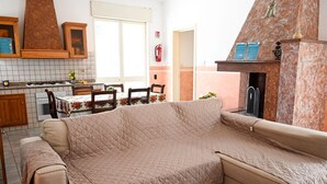 Ein Wohnzimmer mit beiger Couch, ein Essbereich mit Tisch und Stühlen, eine Küche mit Herd, Schränken und Kamin.