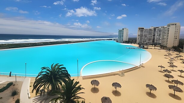 A large swimming pool with a view of the ocean, surrounded by beach umbrellas and palm trees. - Lagoon beach white 311 (La Serena)