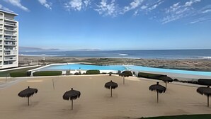 A resort with a pool, beach umbrellas, and a view of the ocean. - Lagoon beach white 311 (La Serena)