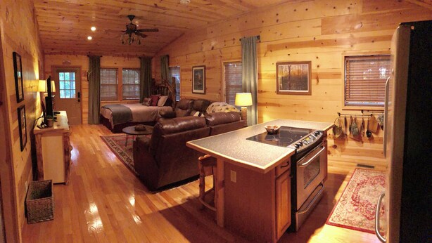 A cozy cabin interior with a dining area, a sofa, a bed, and a kitchen.
