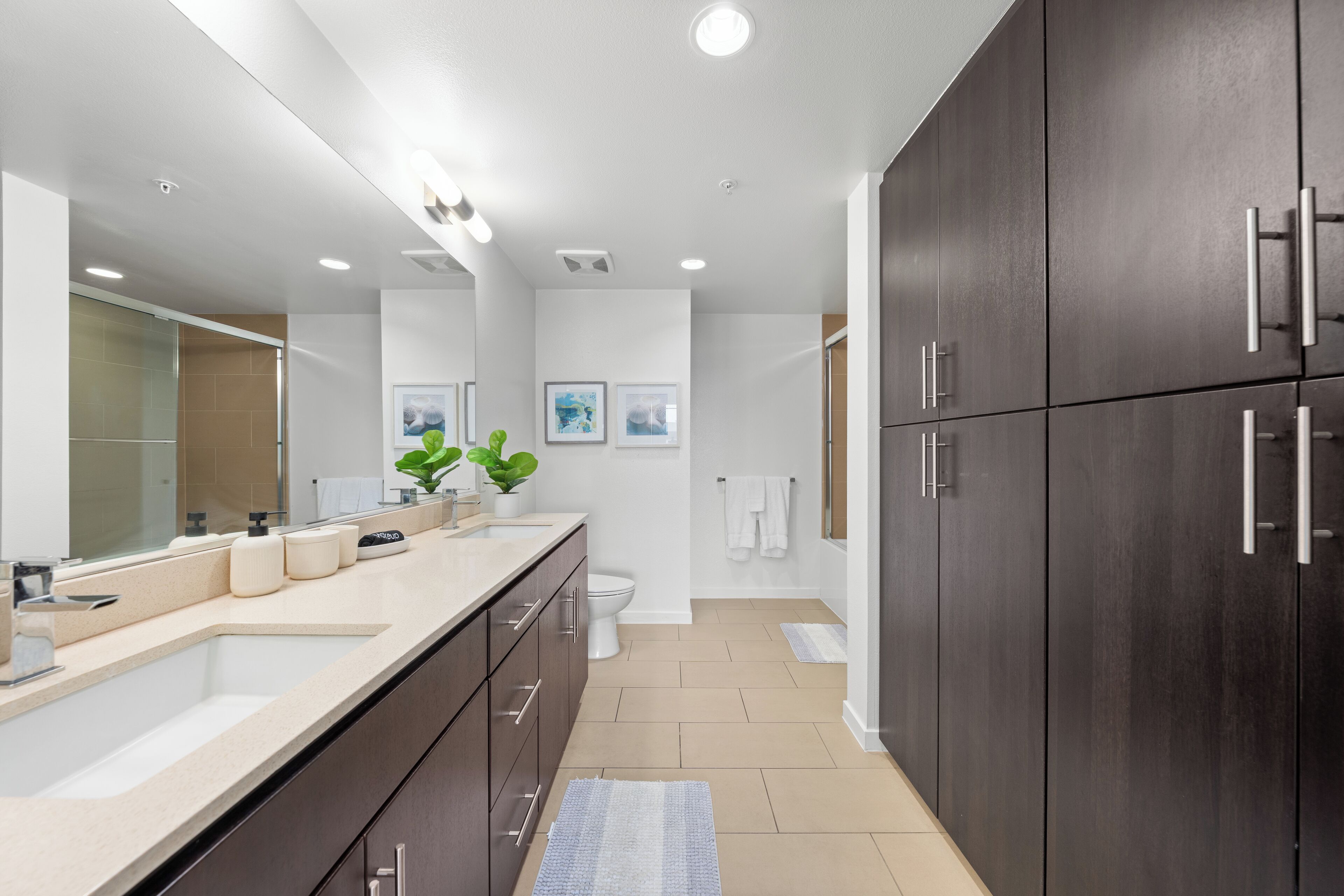 Une salle de bain moderne avec un grand miroir, des meubles sombres et un plan de toilette de couleur beige.