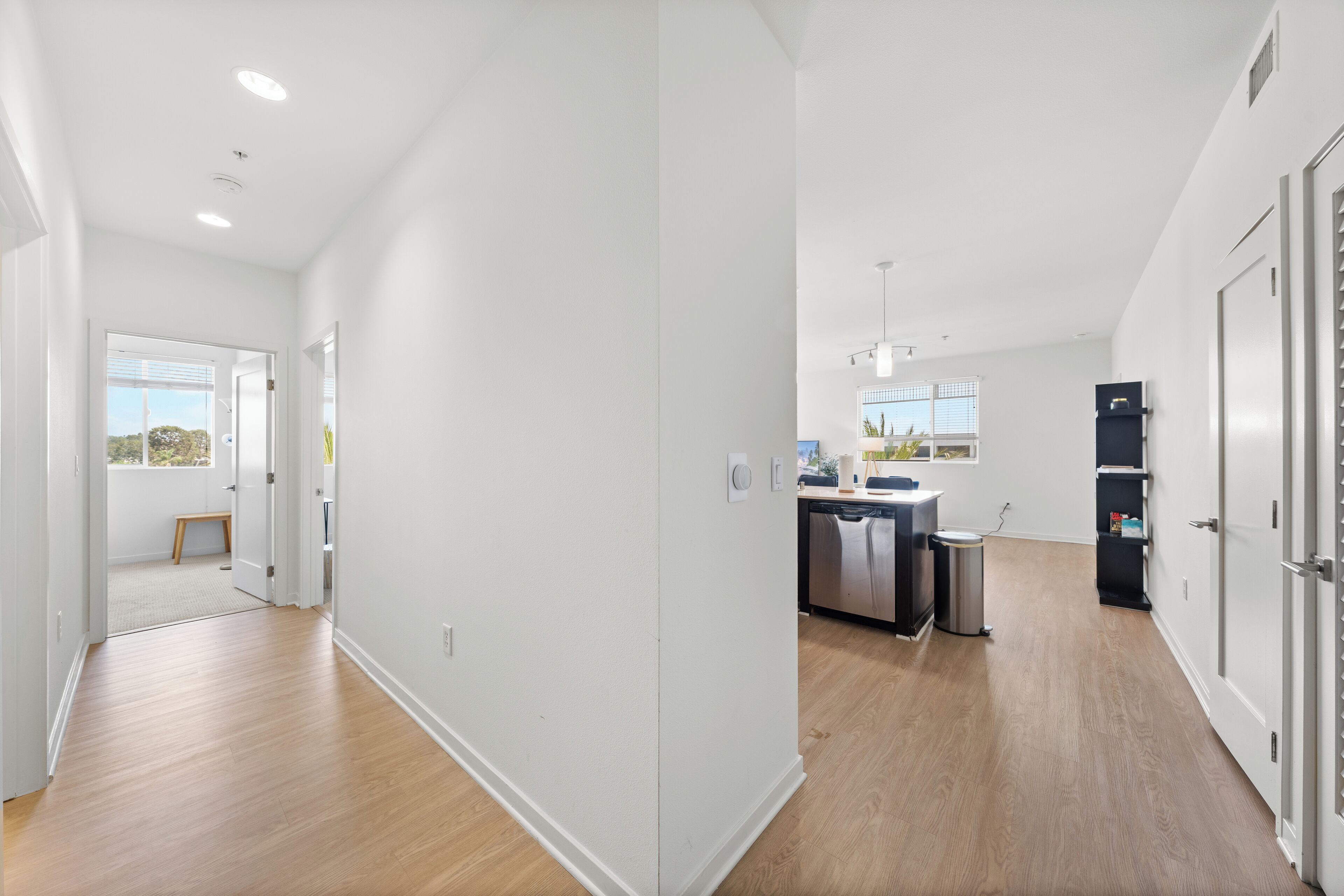 A modern apartment with a kitchen, dining area, and a hallway leading to a balcony.