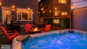 A backyard with a hot tub, outdoor seating, string lights, and a neon sign. - Mayfield Manor-Hot Tub-KingBed-FireTable-BBQ-Wifi (Edmonton)