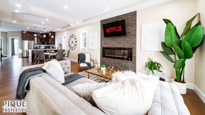 A modern living room with a sofa, coffee table, and a TV mounted on the wall. - Mayfield Manor-Hot Tub-KingBed-FireTable-BBQ-Wifi (Edmonton)