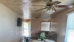 A dining area with a wooden table and chairs, a ceiling fan, and a window with blinds.