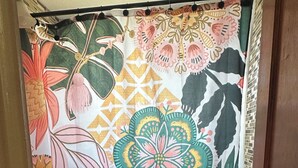 A bathroom with a shower curtain featuring a floral pattern, a white sink, a toilet, and a small rug on the floor.