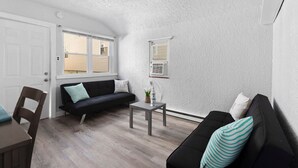 Un espacio habitable compacto con un sofá negro, una mesita y una ventana.