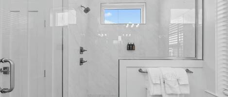 Un espacio de ducha moderno con puerta de cristal, una ventana pequeña y un perchero con toallas blancas.