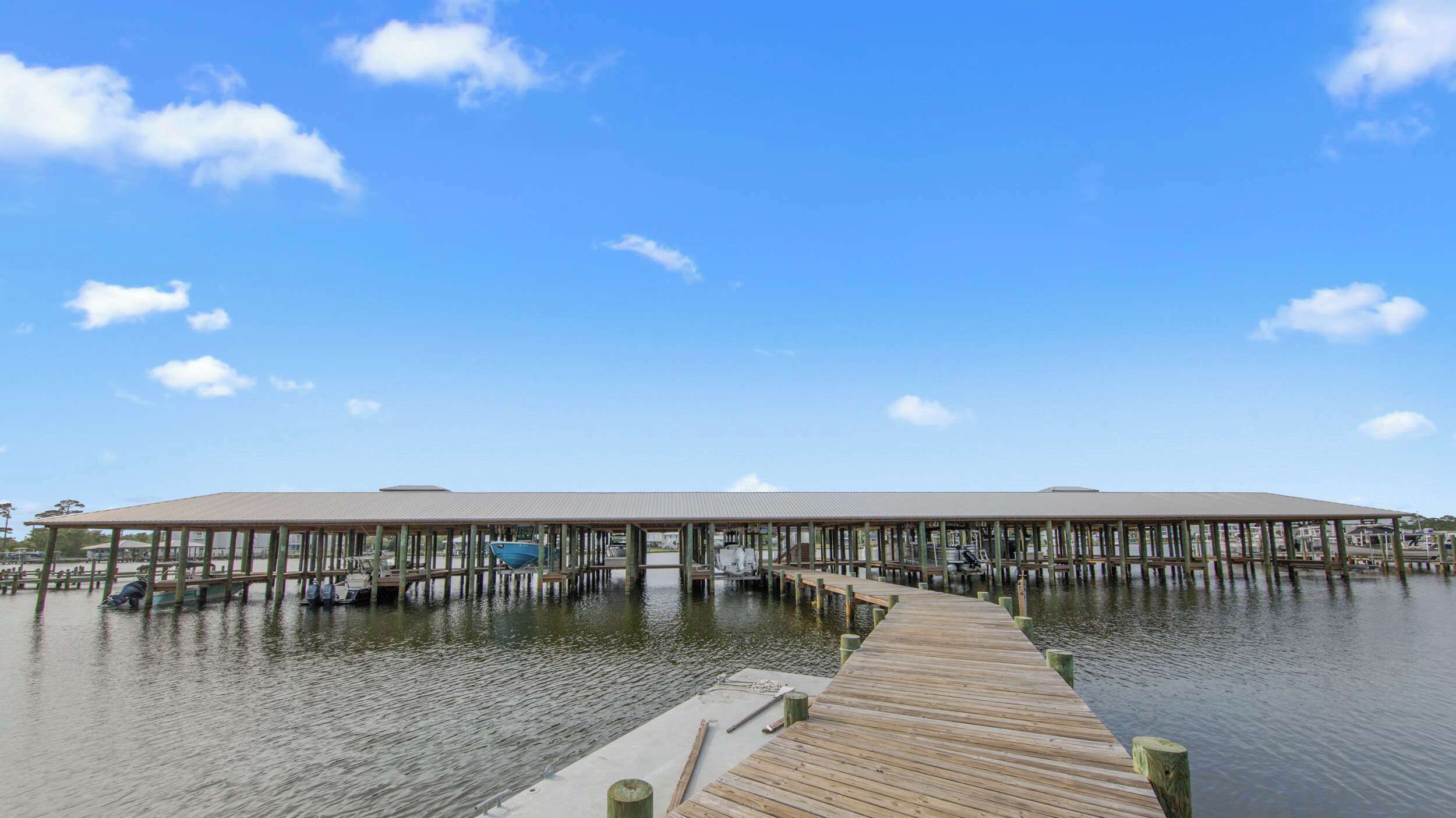 A wooden pier leading to a covered dock area with boats and a clear sky.