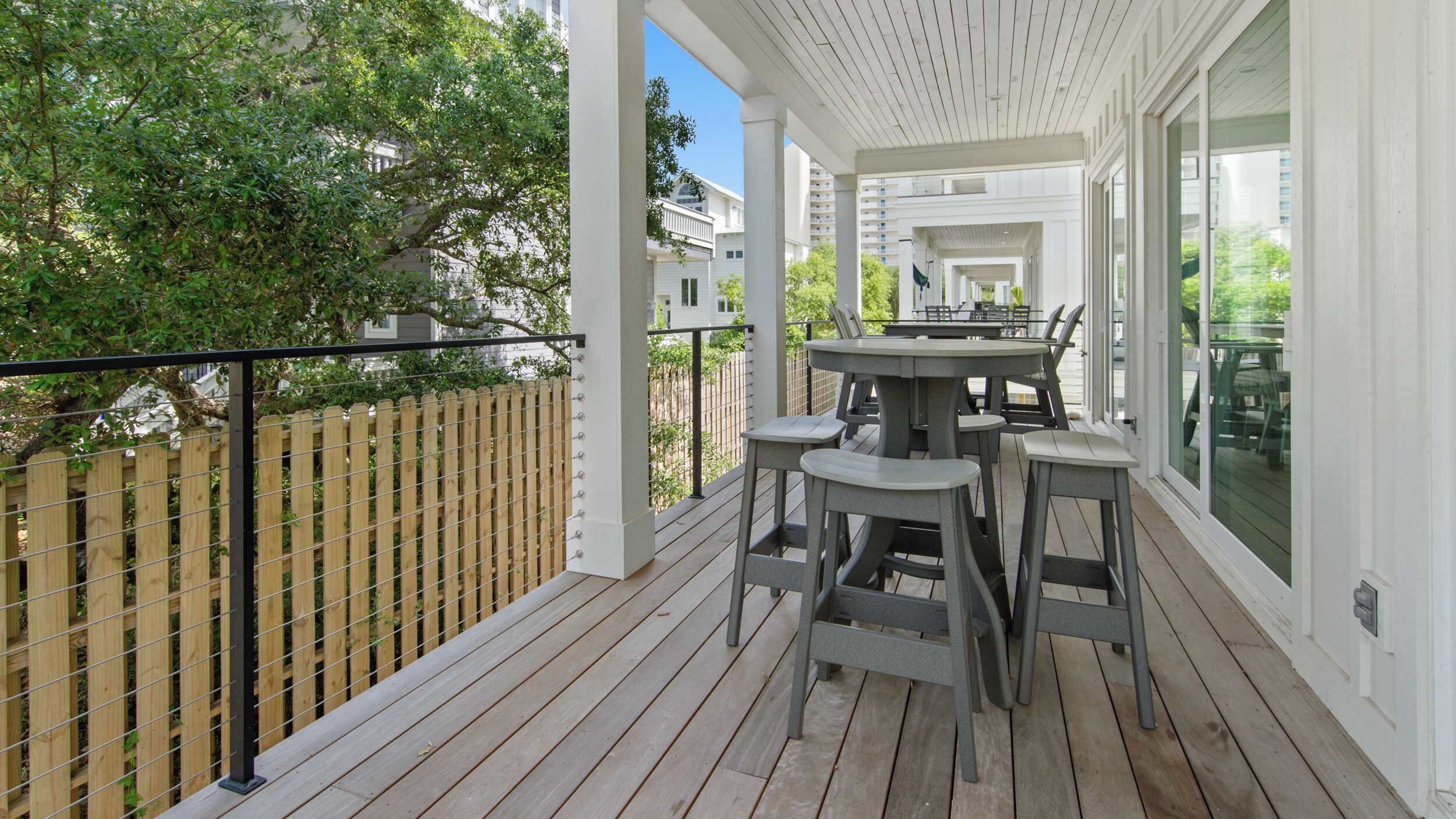 Un patio techado al aire libre con cubierta de madera, una mesa con sillas y vista a una zona residencial.