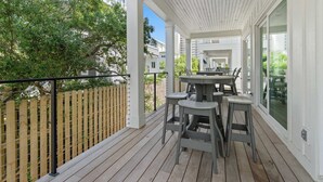 A covered outdoor patio with a wooden deck, a table with chairs, and a view of a residential area. - Dreamy, Accessible Family Home for 12 (Orange Beach)