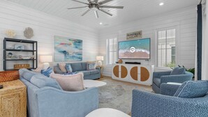 A living room with a grey sofa, blue armchairs, a white entertainment unit, and a ceiling fan. - Dreamy, Accessible Family Home for 12 (Orange Beach)
