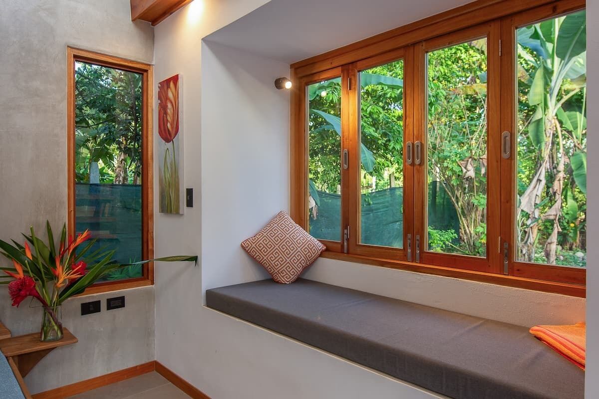A room with a bench by a large window overlooking a garden.