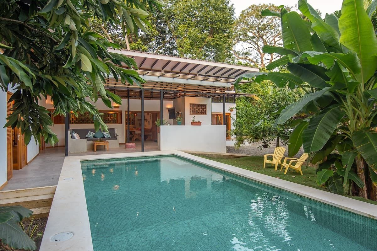 A modern house with a swimming pool, a covered patio, and lush greenery.