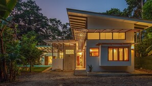 Una casa moderna con un espacio exterior cubierto, rodeada de vegetación.
