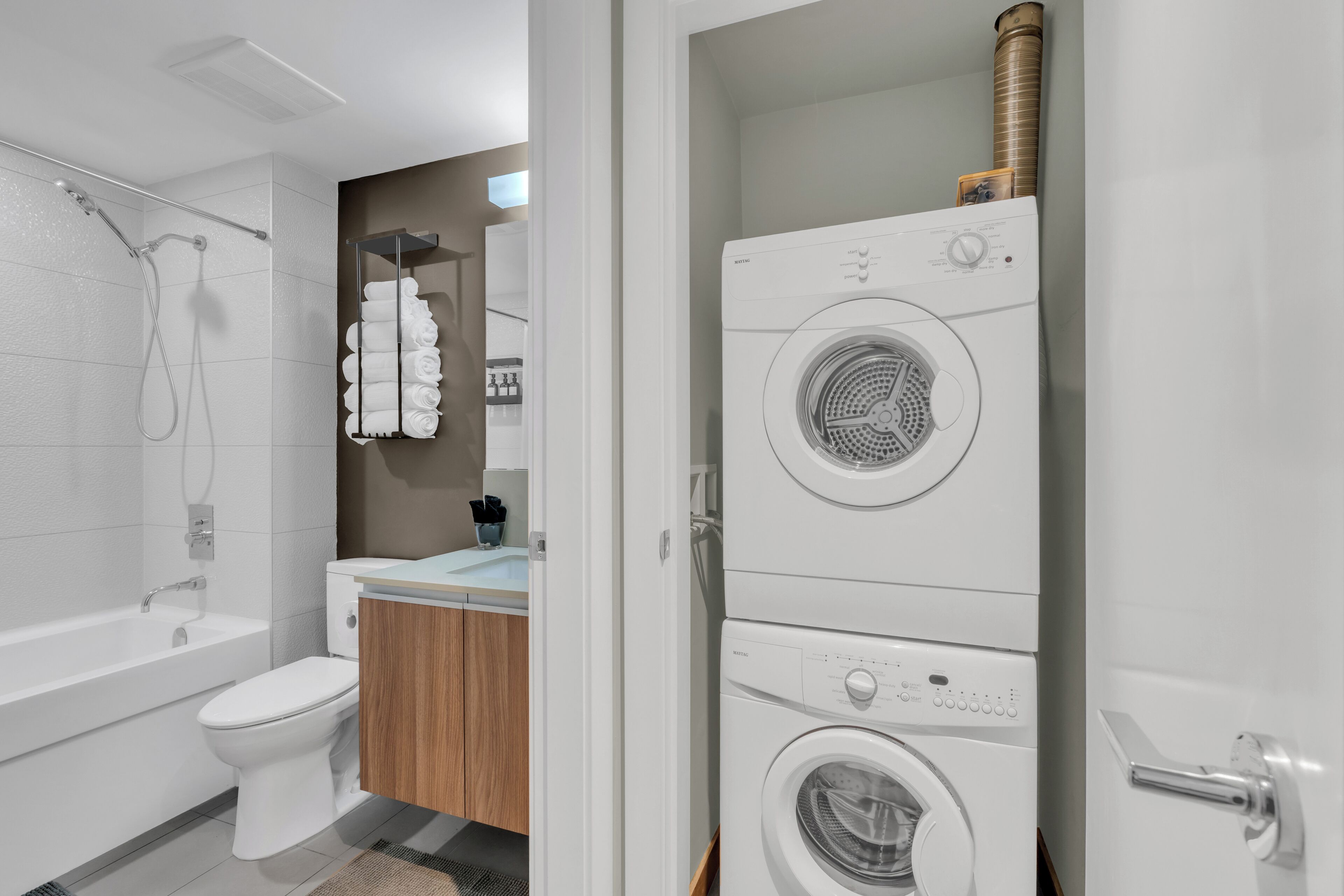 A modern bathroom with a built-in washer and dryer, a toilet, and a shower.
