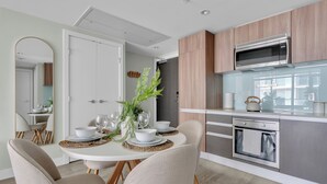 A modern kitchen with a microwave, oven, and wooden cabinets. There is a dining table set with plates, bowls, and glasses. - The Astoria | Steps to Stampede+Saddledome+BMO Center| Free Parking (Calgary)