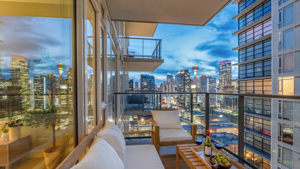 A modern balcony with a city view, a sofa, a dining table with a bottle and fruit, and a plant. - The Astoria | Steps to Stampede+Saddledome+BMO Center| Free Parking (Calgary)