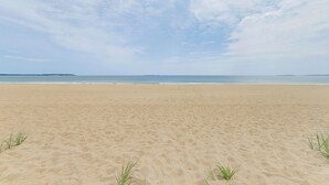 Ein weiter Sandstrand mit blauem Himmel und ruhiger See.