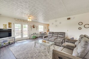 A living room with a large gray sectional sofa, a glass coffee table, a flat-screen TV, and a ceiling fan.