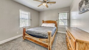 Een slaapkamer met een houten bed, een plafondventilator, twee ramen met zonwering en een dressoir.