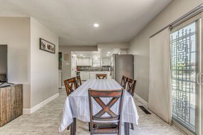 Un'area pranzo con tavolo e sedie, una cucina sullo sfondo e una porta scorrevole in vetro con cancello in metallo.