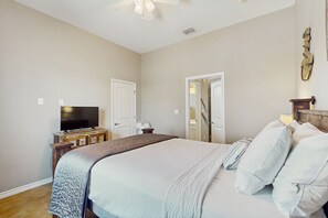 A bedroom with a bed, a television, a wooden dresser, and a door leading to another room. - Coastal, dog-friendly townhouse with shared pool & large yard - steps to sand (Corpus Christi)