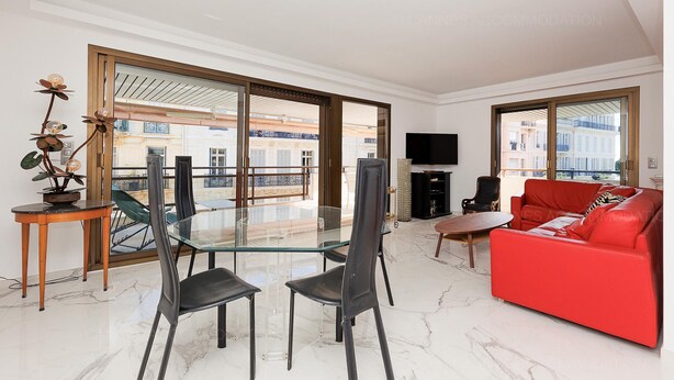 Ein modernes Wohnzimmer mit einem Glastisch, einem roten Sofa und großen Fenstern mit Blick auf Gebäude.