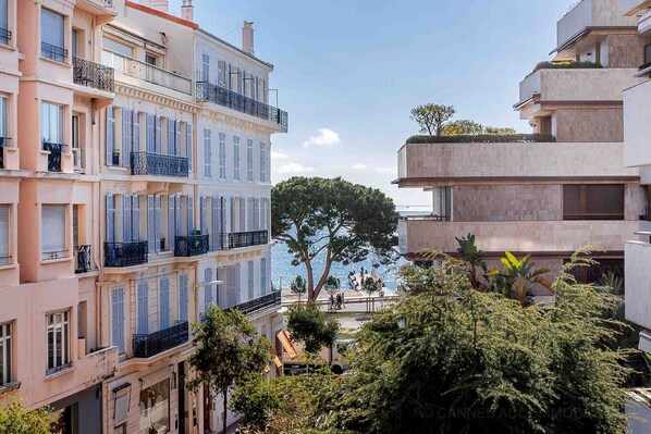A multi-story building with balconies, a tree in the foreground, and a view of the sea.