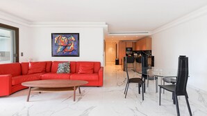 Ein modernes Wohnzimmer mit einem roten Sofa, einem Glastisch und einer Küche im Hintergrund.