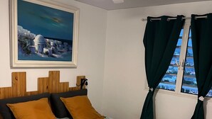 A bedroom with a bed, a ceiling fan, a painting, and a window with curtains. - Appart Anse à l'Ane, Les Trois Ilets, with panoramic view 300 m from the sea (LES TROIS ILETS)