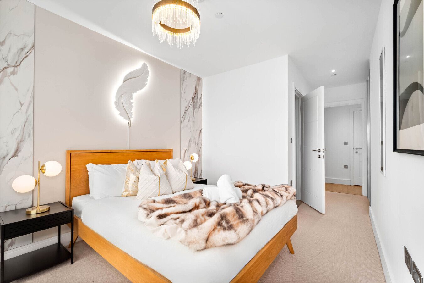 A modern bedroom with a wooden bed, marble walls, a chandelier, and a fluffy blanket.