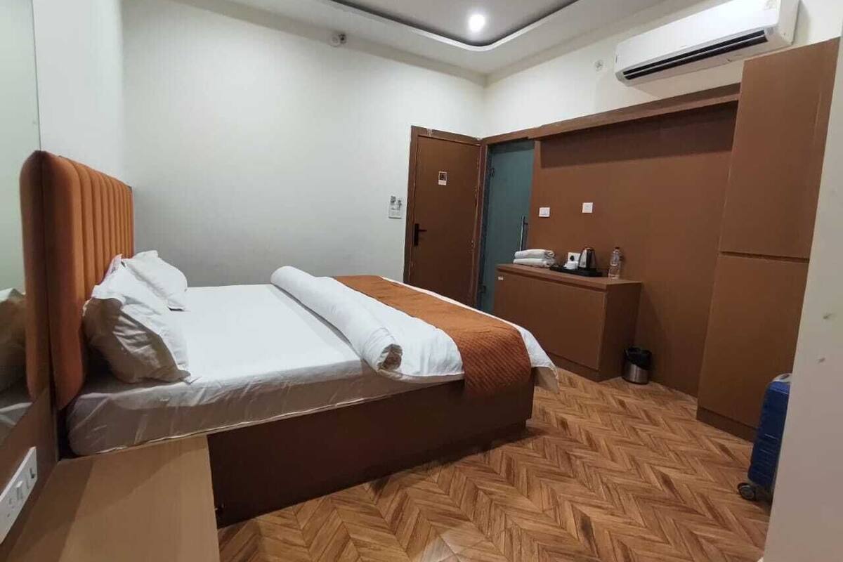 Hotellihuone, jossa on sänky, puulattia, työpöytä ja ilmastointilaite.