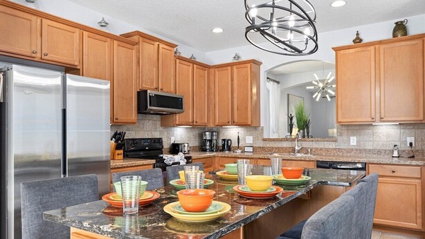 A modern kitchen with wooden cabinets, a stainless steel refrigerator, a granite countertop, and a central island with seating. - Luxury 2850sf Rental | Water + Conservation Views | Near Clubhouse | Gated (Davenport)