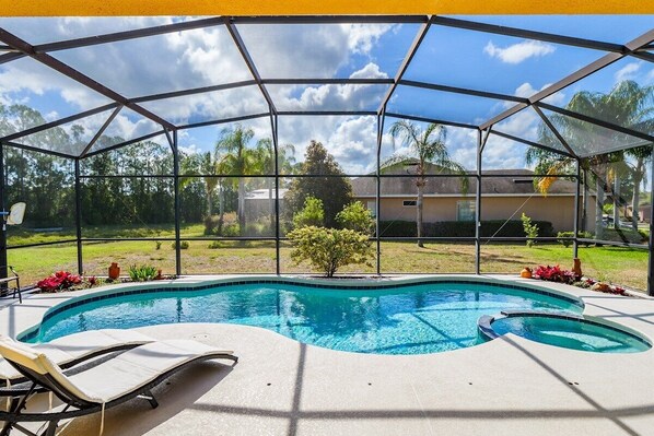 Una piscina techada con sillas de descanso, rodeada por un recinto de vidrio, con vista a una zona residencial con árboles y casas.