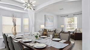 A dining room with a wooden table set for four, flanked by two windows with white curtains. - Luxury 2850sf Rental | Water + Conservation Views | Near Clubhouse | Gated (Davenport)