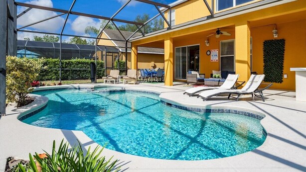 A pool area with a covered section, lounge chairs, and a yellow building. - Luxury 2850sf Rental | Water + Conservation Views | Near Clubhouse | Gated (Davenport)