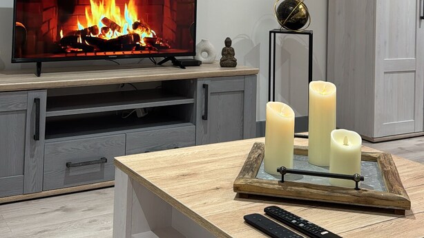 A living room with a fireplace, a clock, a cabinet, and a coffee table with candles and remote controls.