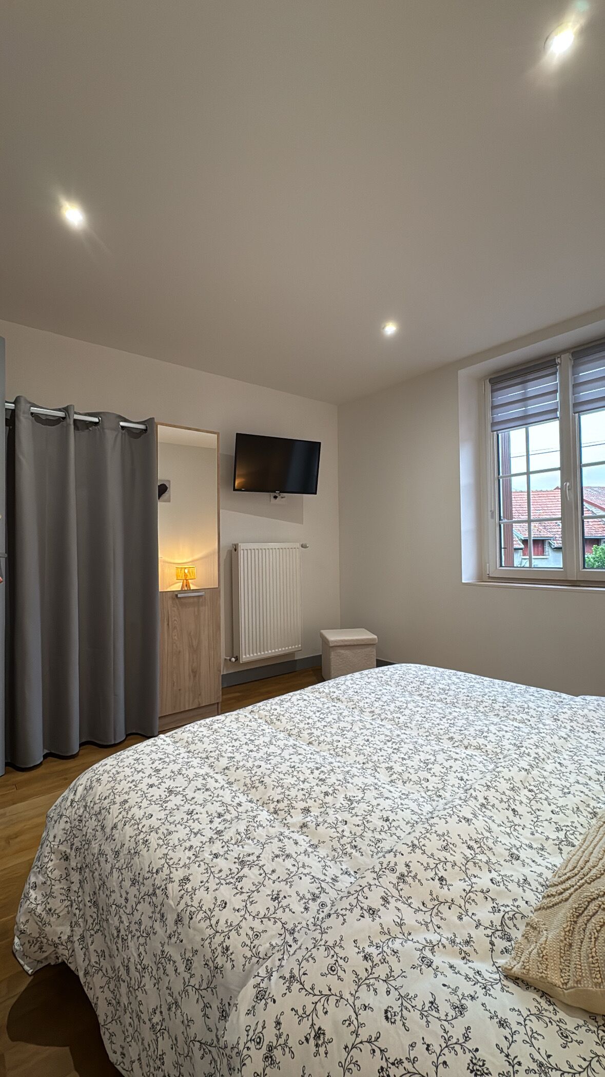 A bedroom with a bed, a TV mounted on the wall, a window, and a radiator.