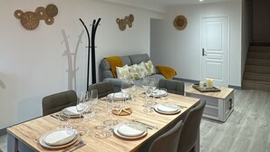 A modern dining area with a wooden table set for four, a grey sofa with cushions, and decorative wall art.