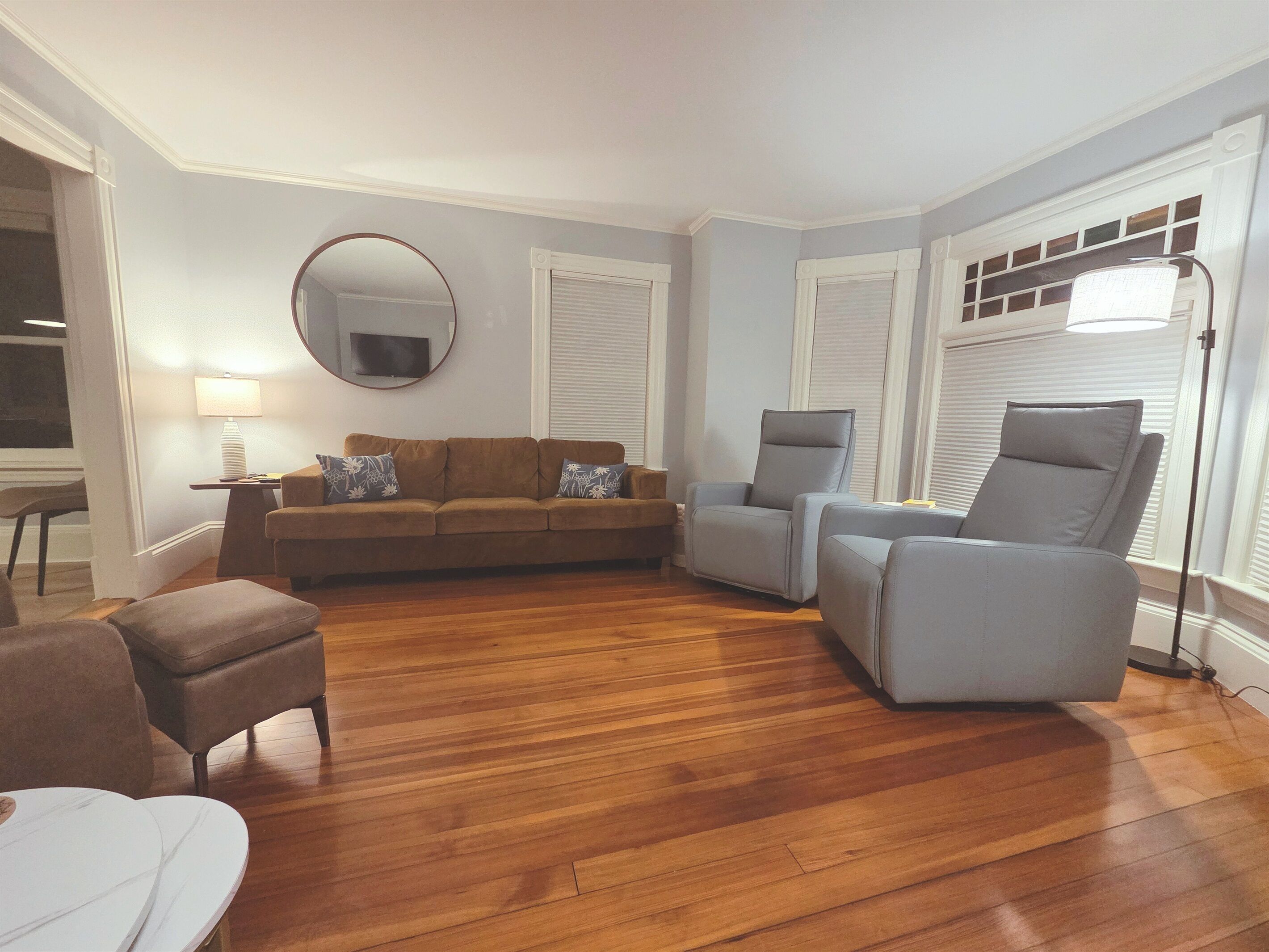 Ein Wohnzimmer mit einem braunen Sofa, zwei Sesseln, einem runden Spiegel und einer Lampe.