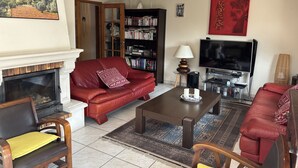 Un salón con chimenea, sofá de cuero rojo, una mesa de centro, una estantería y un televisor.